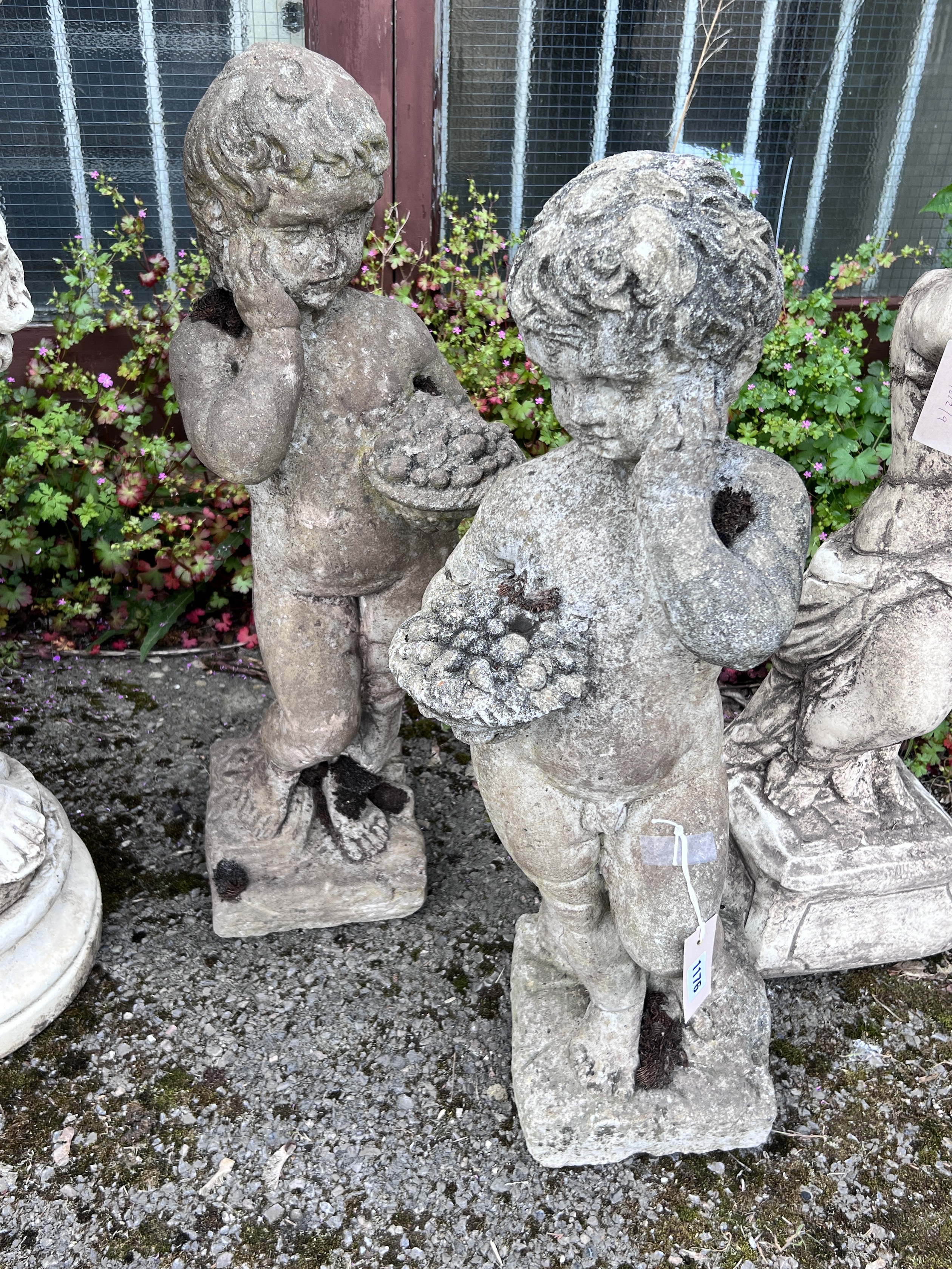 A pair of reconstituted stone garden ornaments, cherubs with fruit baskets, height 72cm